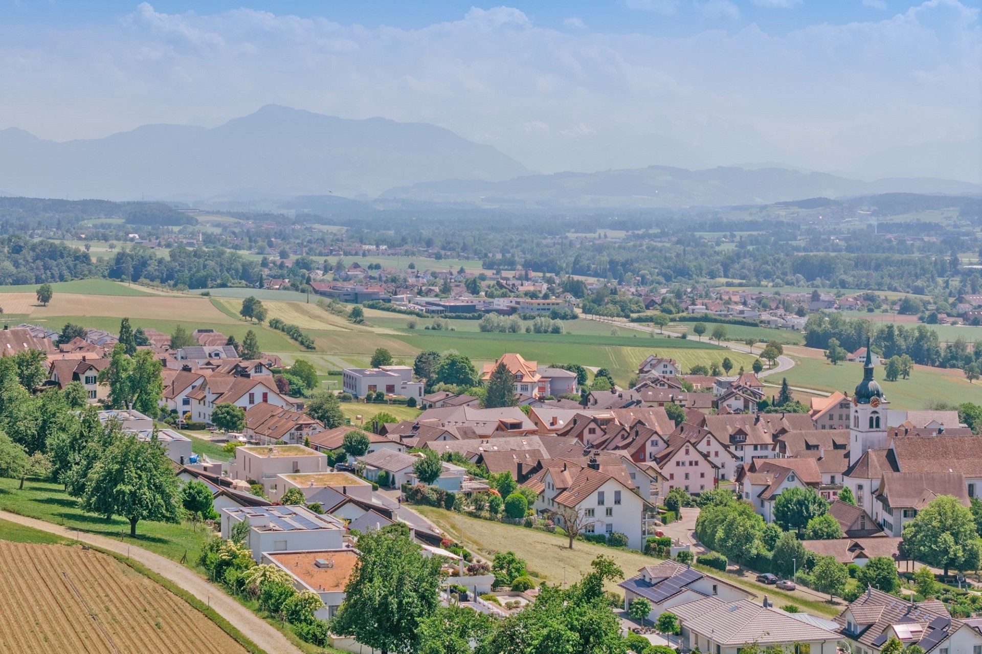 Panoramablick über ein Dorf im Grünen mit Alpenkulisse