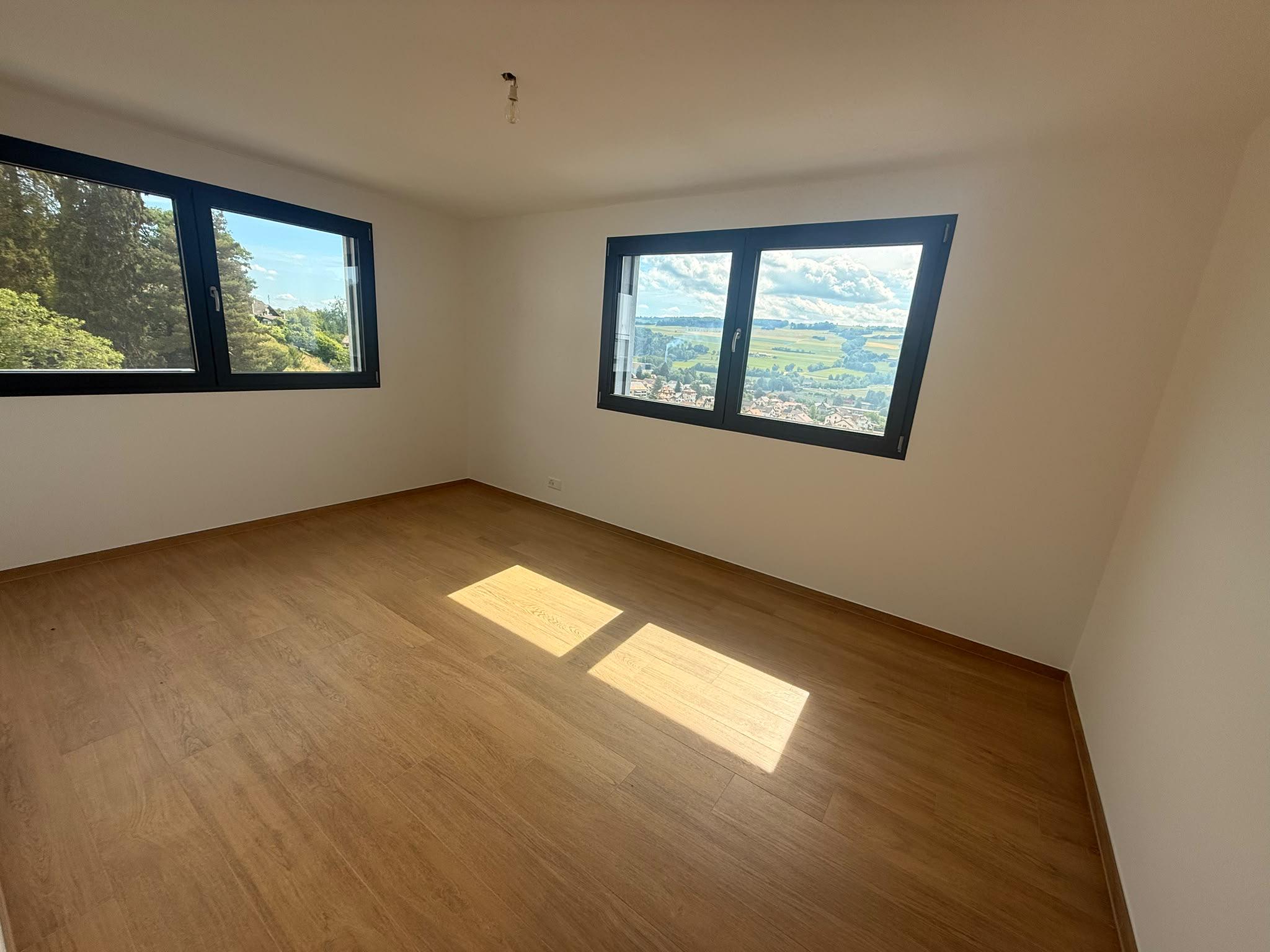 Heller leerer Wohnraum mit zwei Fenstern und Holzboden