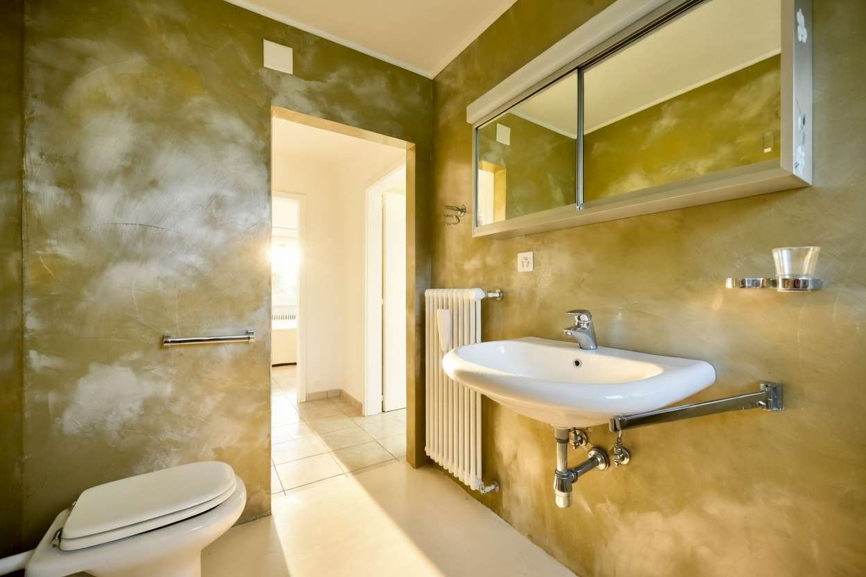 Modernes Badezimmer mit grünlich-goldener Spachtelwand und Spiegelschrank