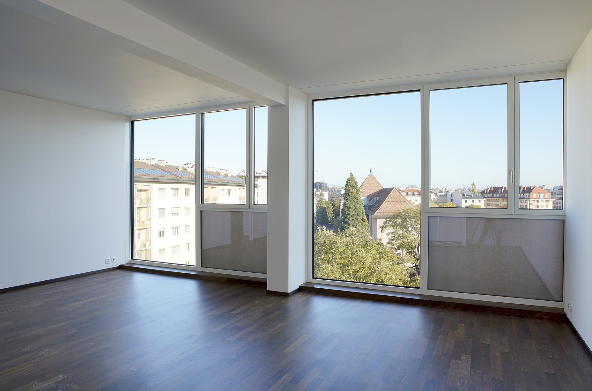 Heller leerer Wohnraum mit großflächigen Fenstern und Stadtblick