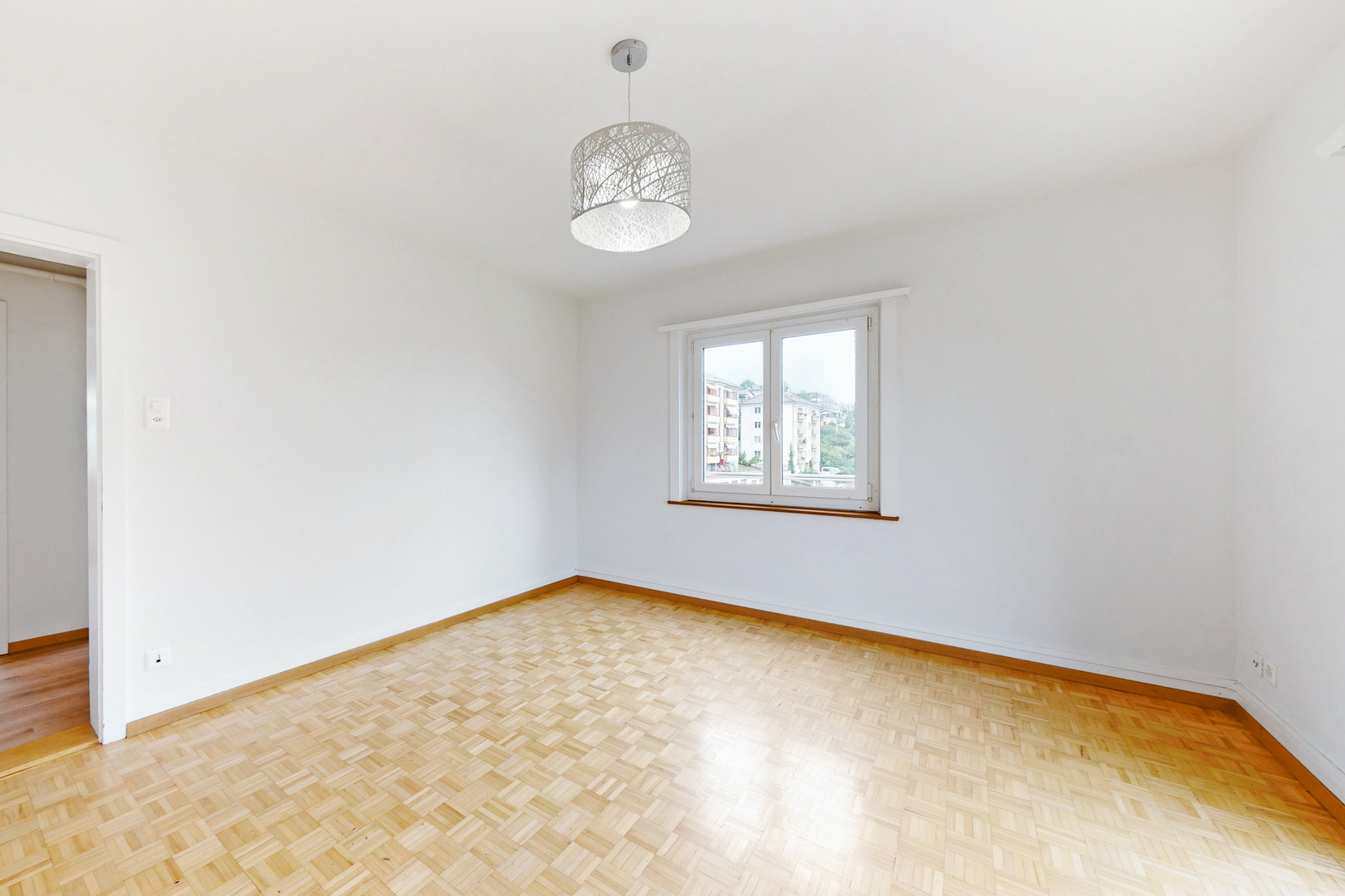 Helles, leeres Zimmer mit Parkettboden und Fenster