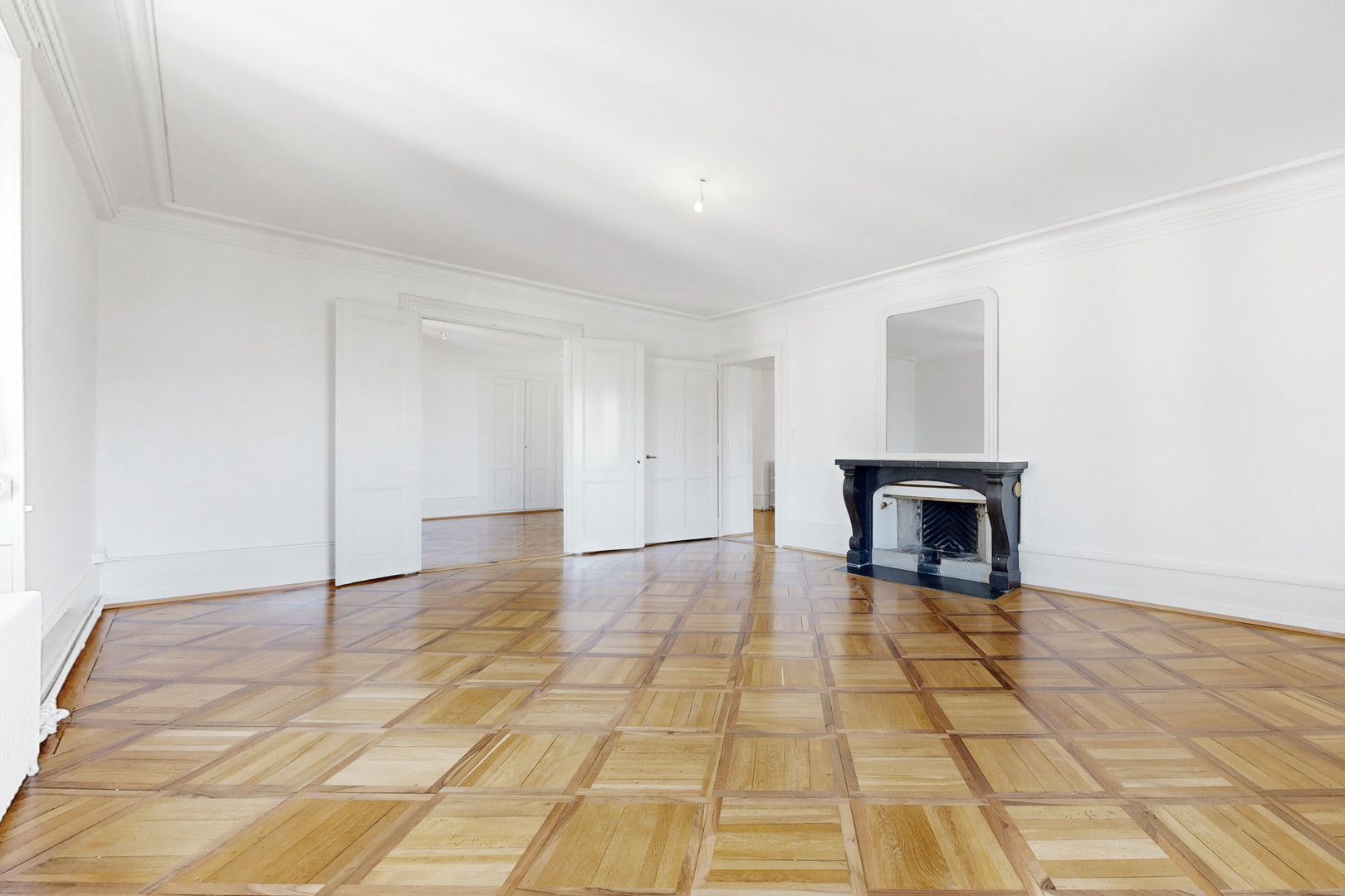 Großer leerer Altbau-Wohnraum mit Kassettenparkett und Kamin