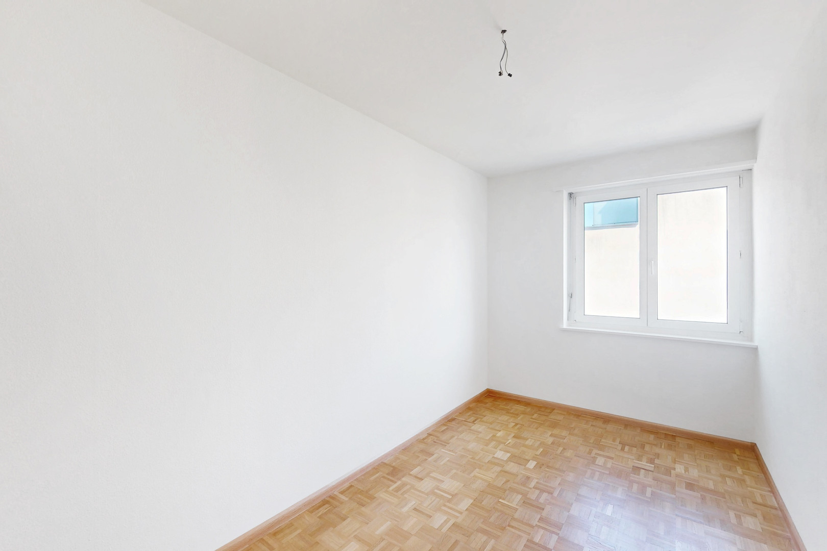Helles, leeres Zimmer mit Parkett und Fenster