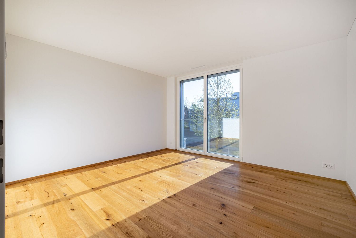 Heller leerer Raum mit Holzparkett und Balkonzugang