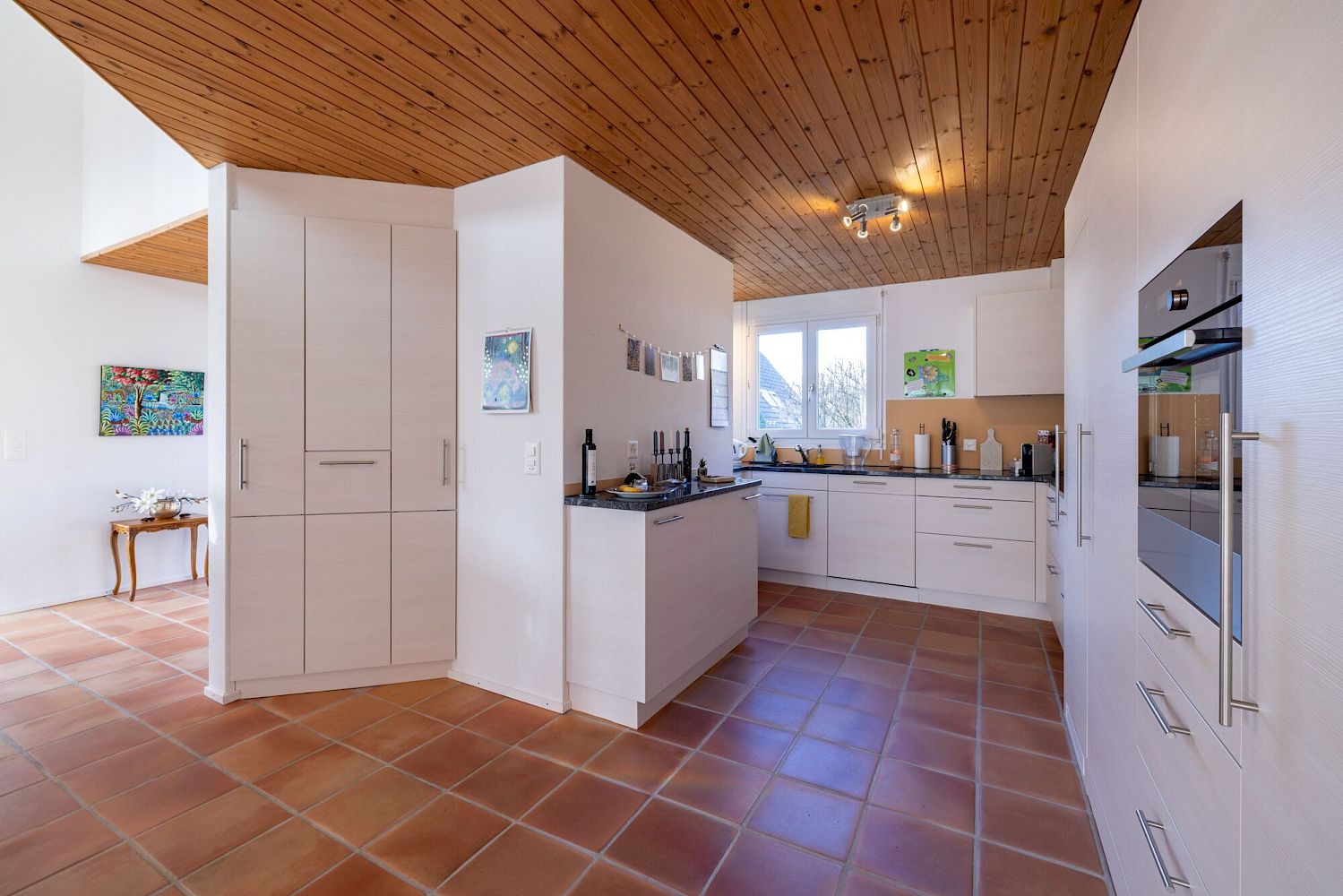 Offene Küche mit terrakottafarbenem Fliesenboden und Holzdecke