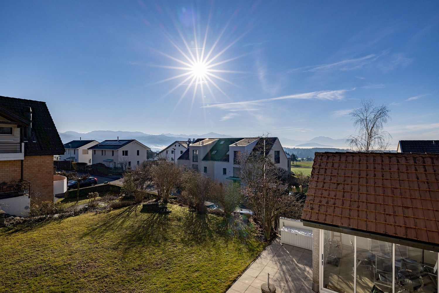 Blick über Wohnhäuser und Garten mit Bergpanorama
