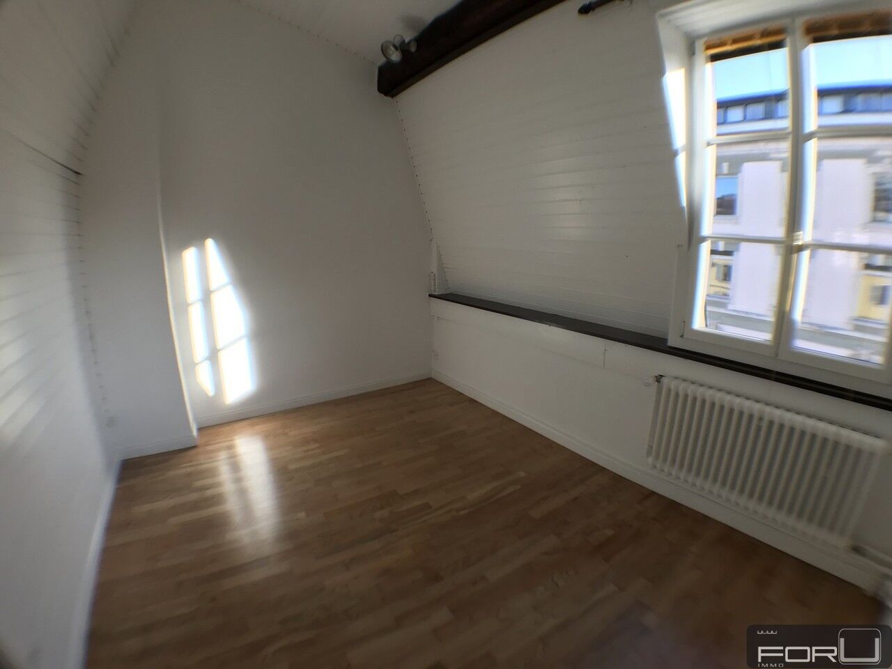 Helles, leeres Zimmer mit Holzfußboden und großem Fenster