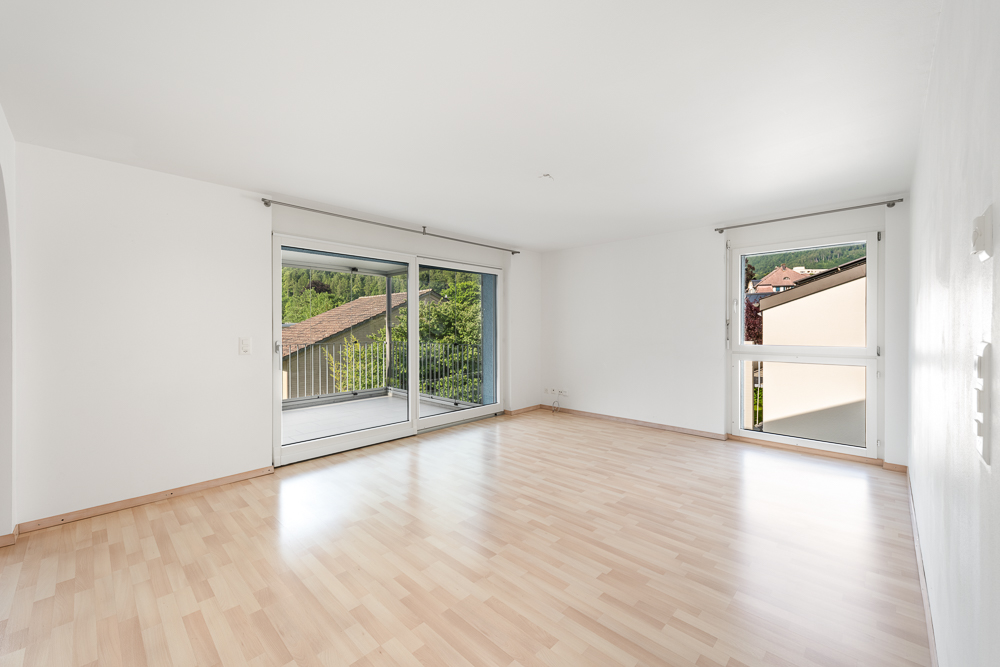 Heller leerer Wohnraum mit Balkon und großen Fenstern