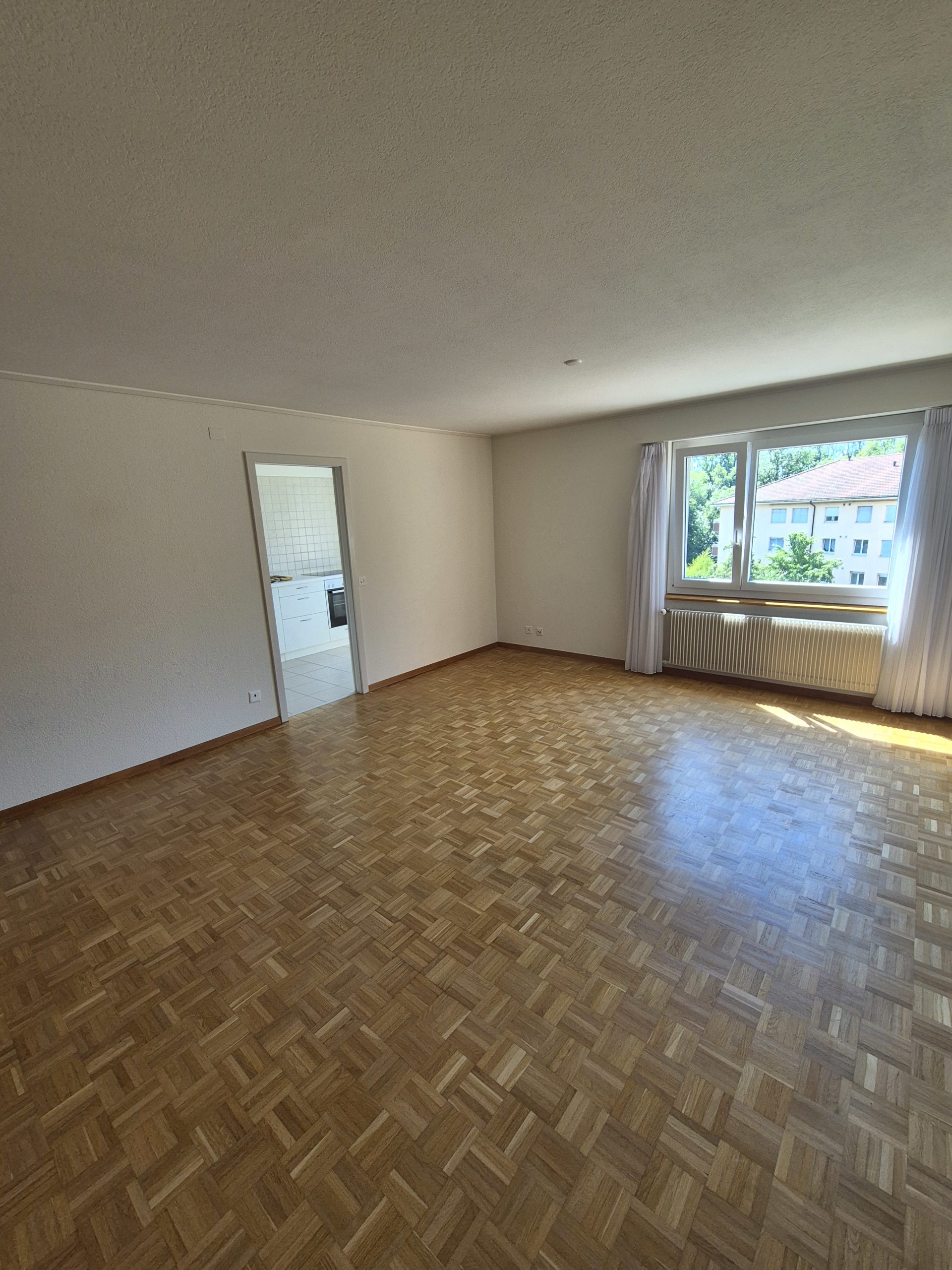 Leeres Wohnzimmer mit Parkettboden und Fensterblick