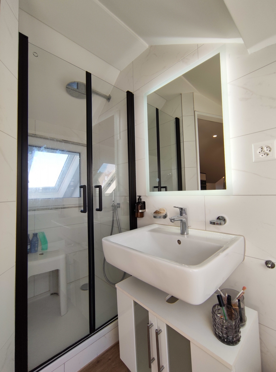Modernes Badezimmer mit Glasdusche und beleuchtetem Spiegel