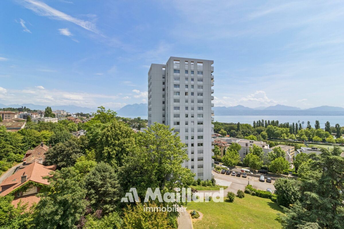 Blick über Stadt, Grünflächen und See mit hohem Wohngebäude