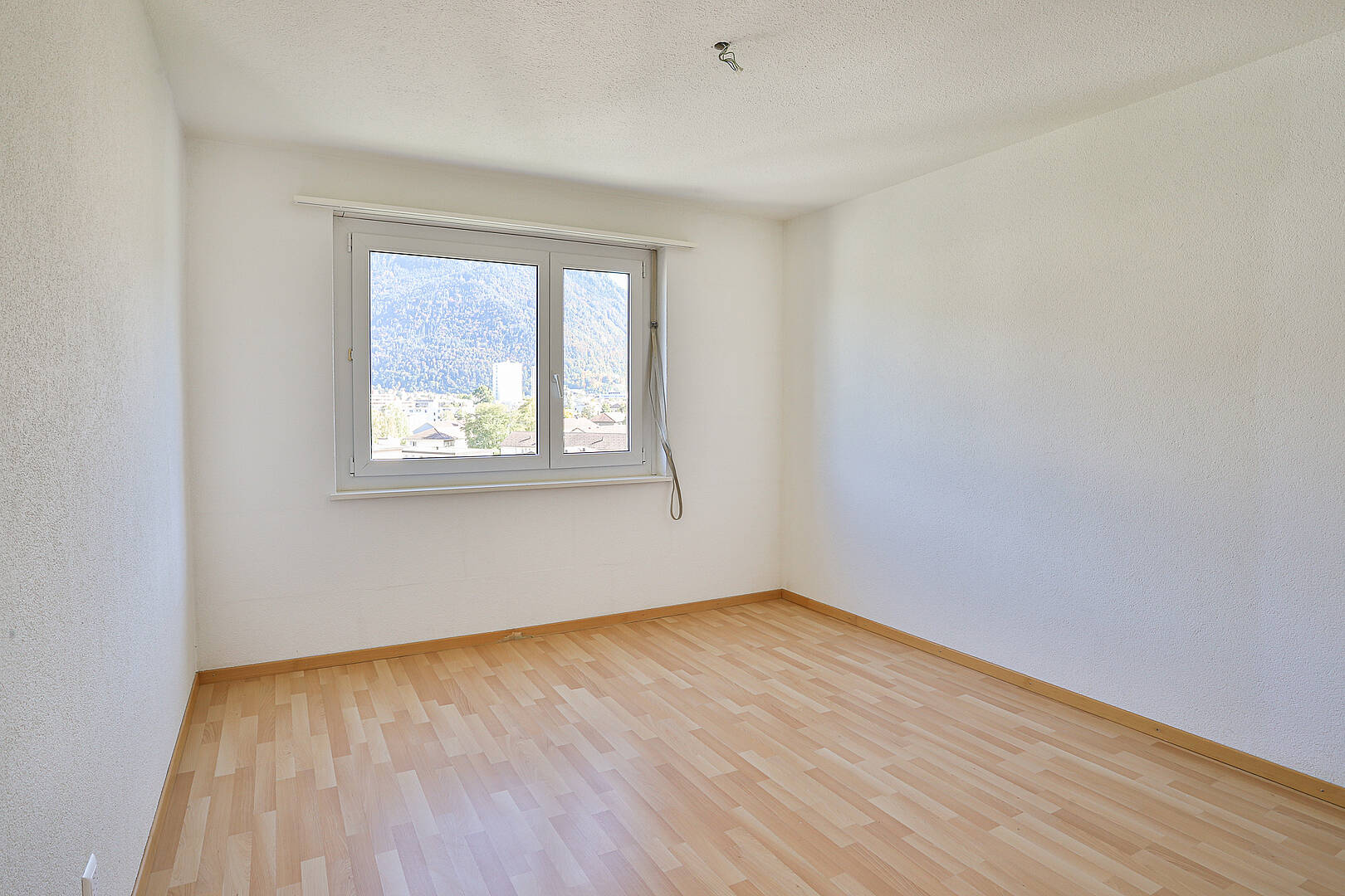 Leerer heller Raum mit Fenster und Holzoptikboden
