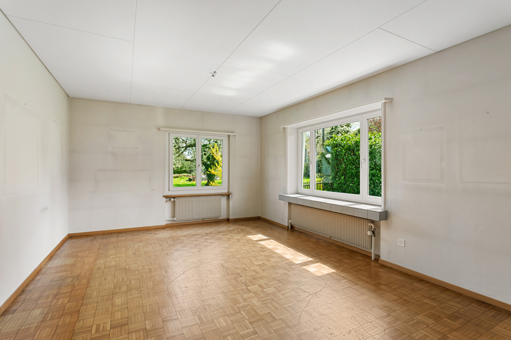 Leerer Wohnraum mit Parkett und großen Fenstern