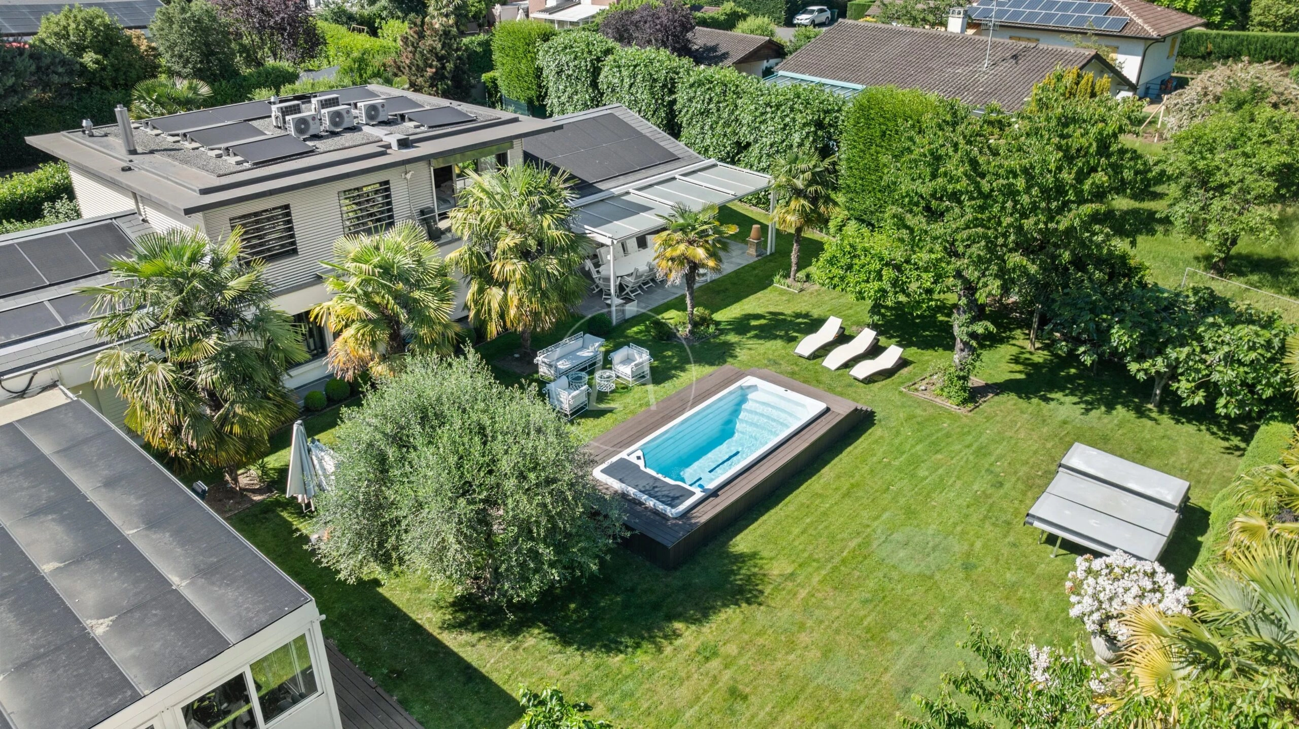 Luftaufnahme eines modernen Hauses mit großem Garten, Pool und Solardächern
