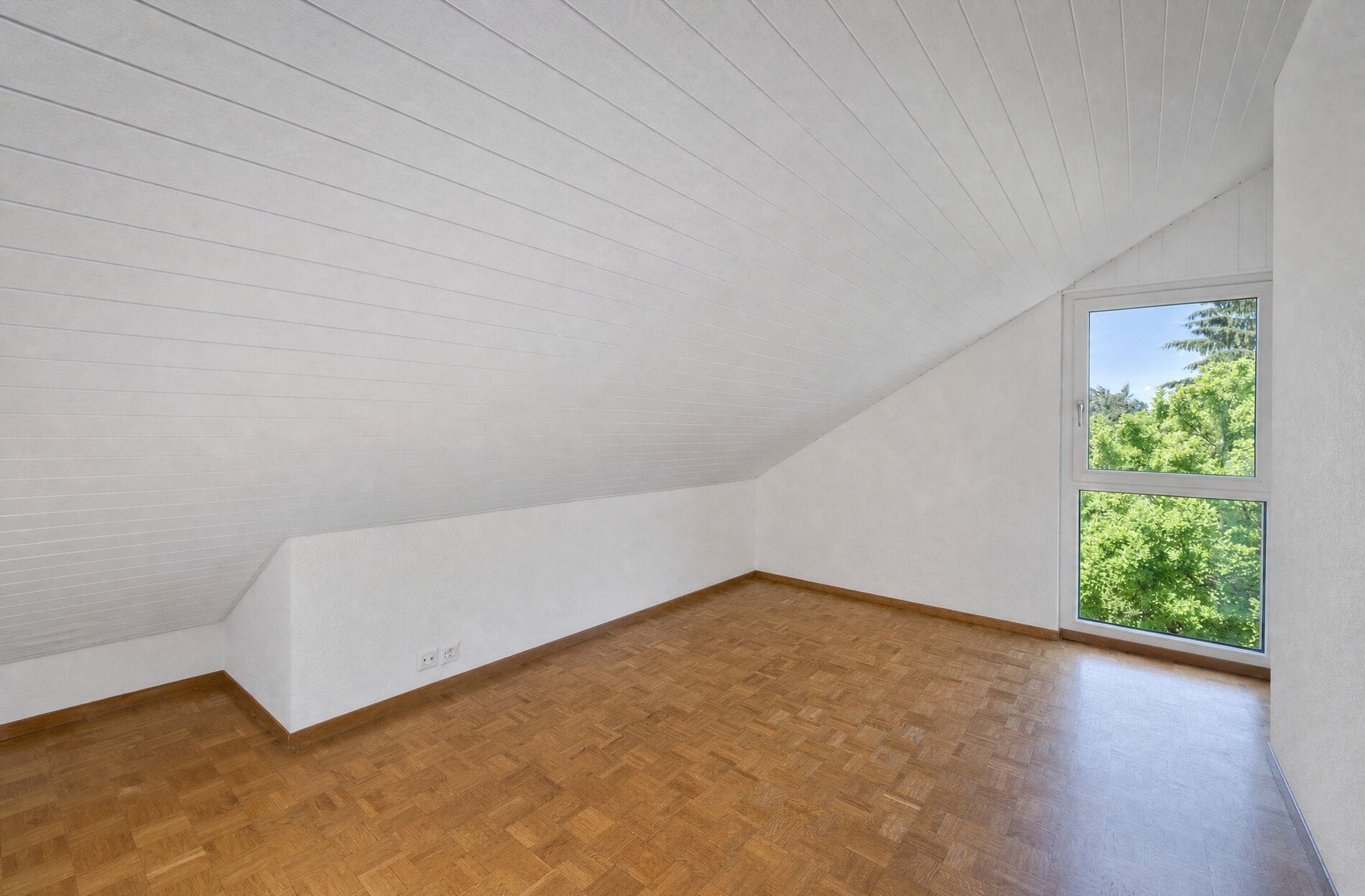 Leerer Dachgeschossraum mit Fensterblick ins Grüne
