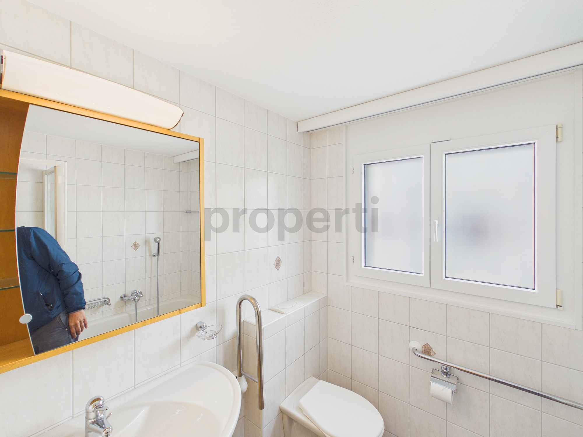 Kleines weiß gefliestes Badezimmer mit Fenster und Spiegel