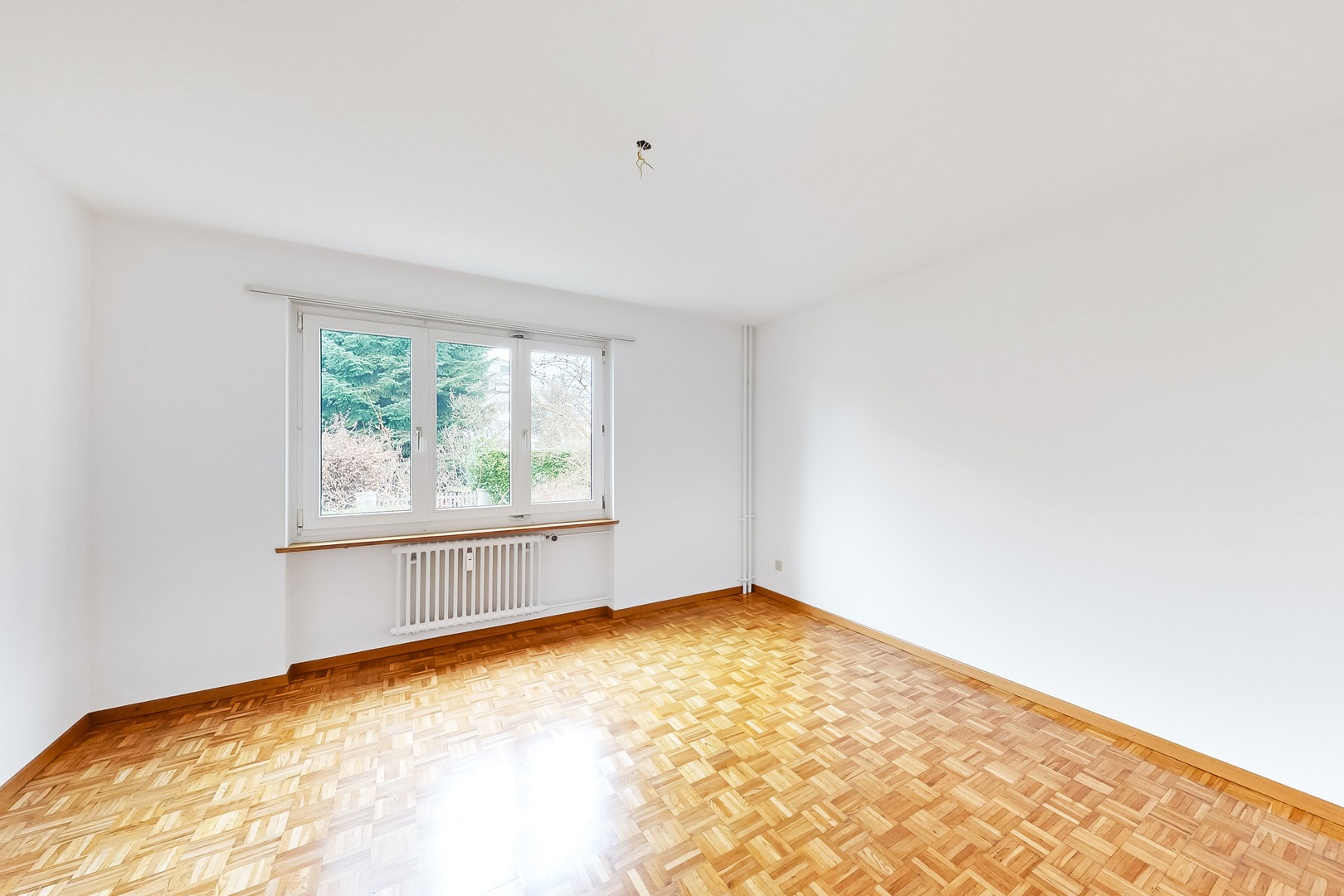 Helles, leeres Zimmer mit Parkettboden und Fenster