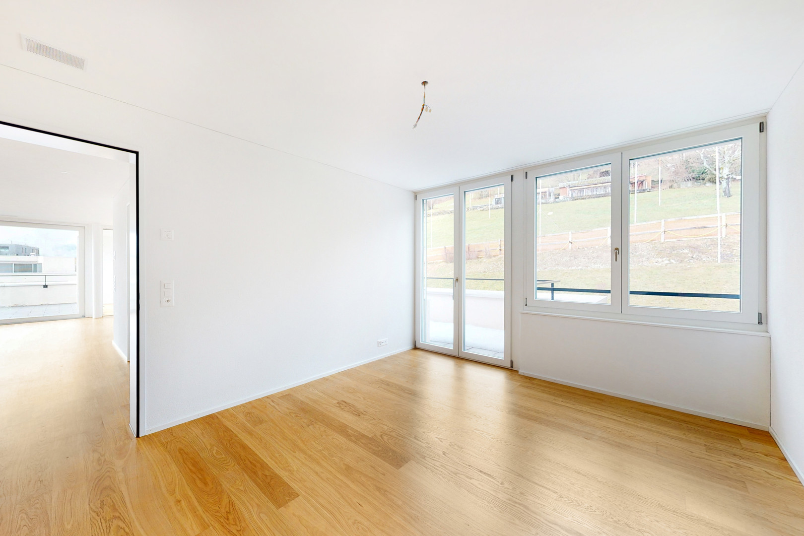 Heller leerer Raum mit Holzfußboden und großen Fenstern