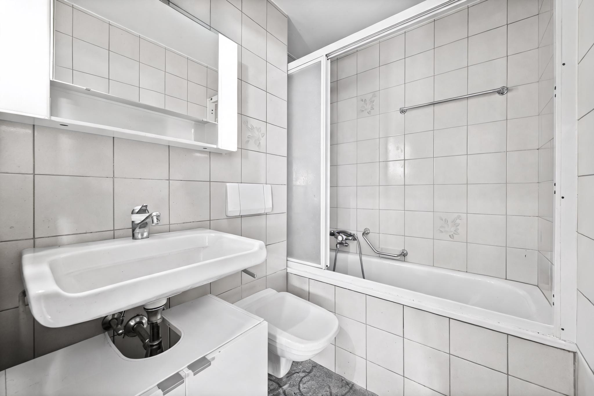 Kleines weiß gefliestes Badezimmer mit Wanne und Waschbecken