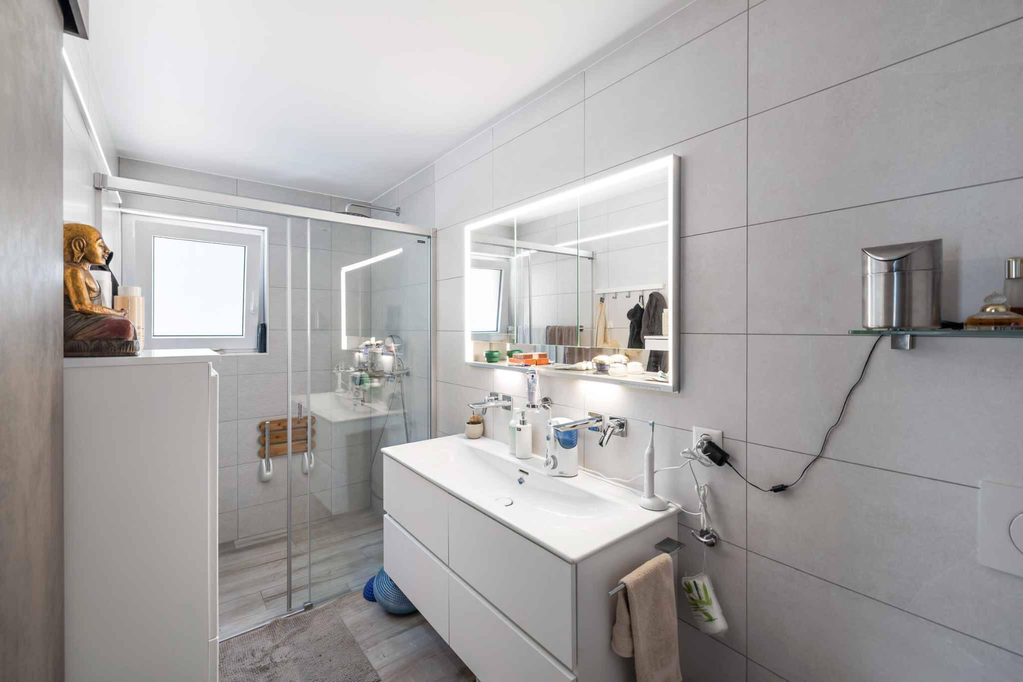 Modernes Badezimmer mit Glasdusche und beleuchtetem Spiegel