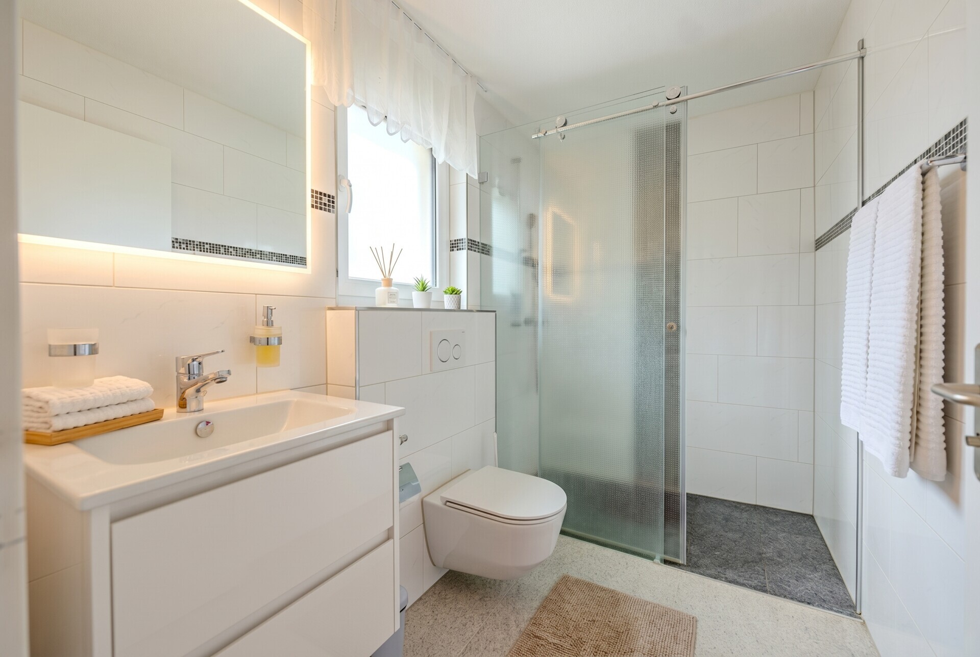 Modernes Badezimmer mit Glasdusche und beleuchtetem Spiegel
