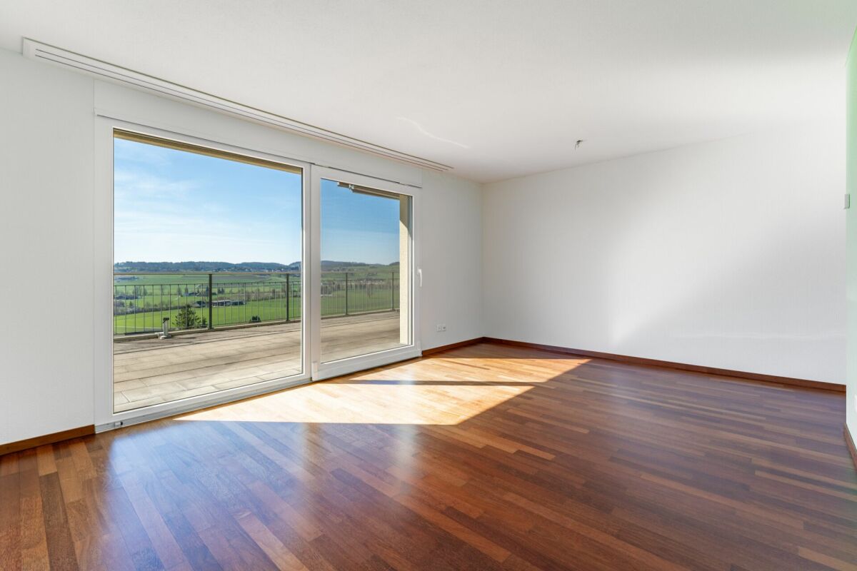 Leerer Wohnraum mit großer Glasfront und Balkonblick