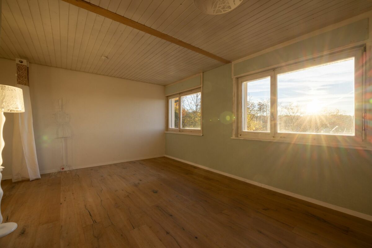 Leerer, heller Wohnraum mit großen Fenstern und Holzboden