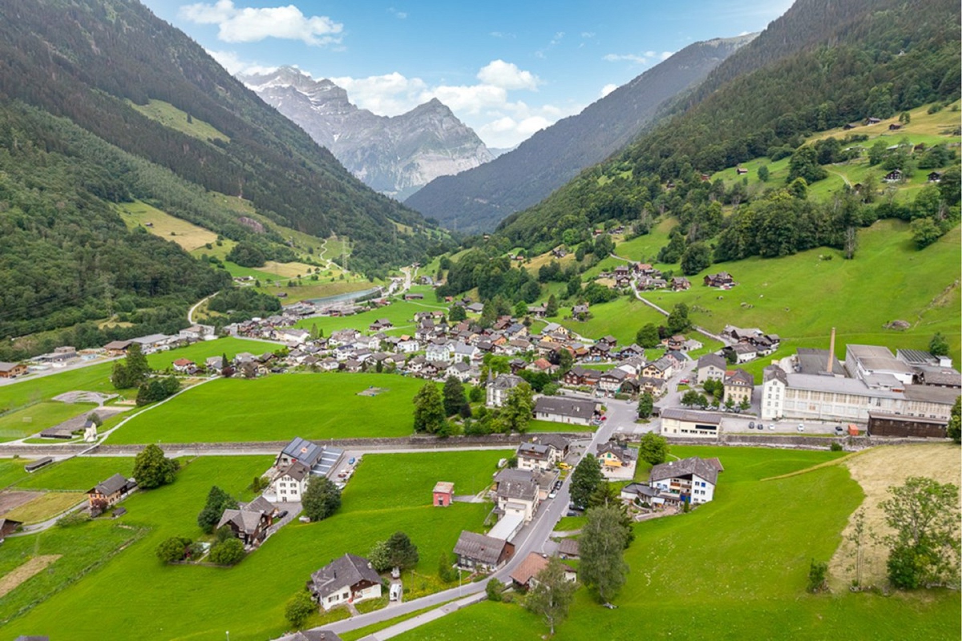 Luftaufnahme eines alpinen Tals mit Dorf und Bergkulisse