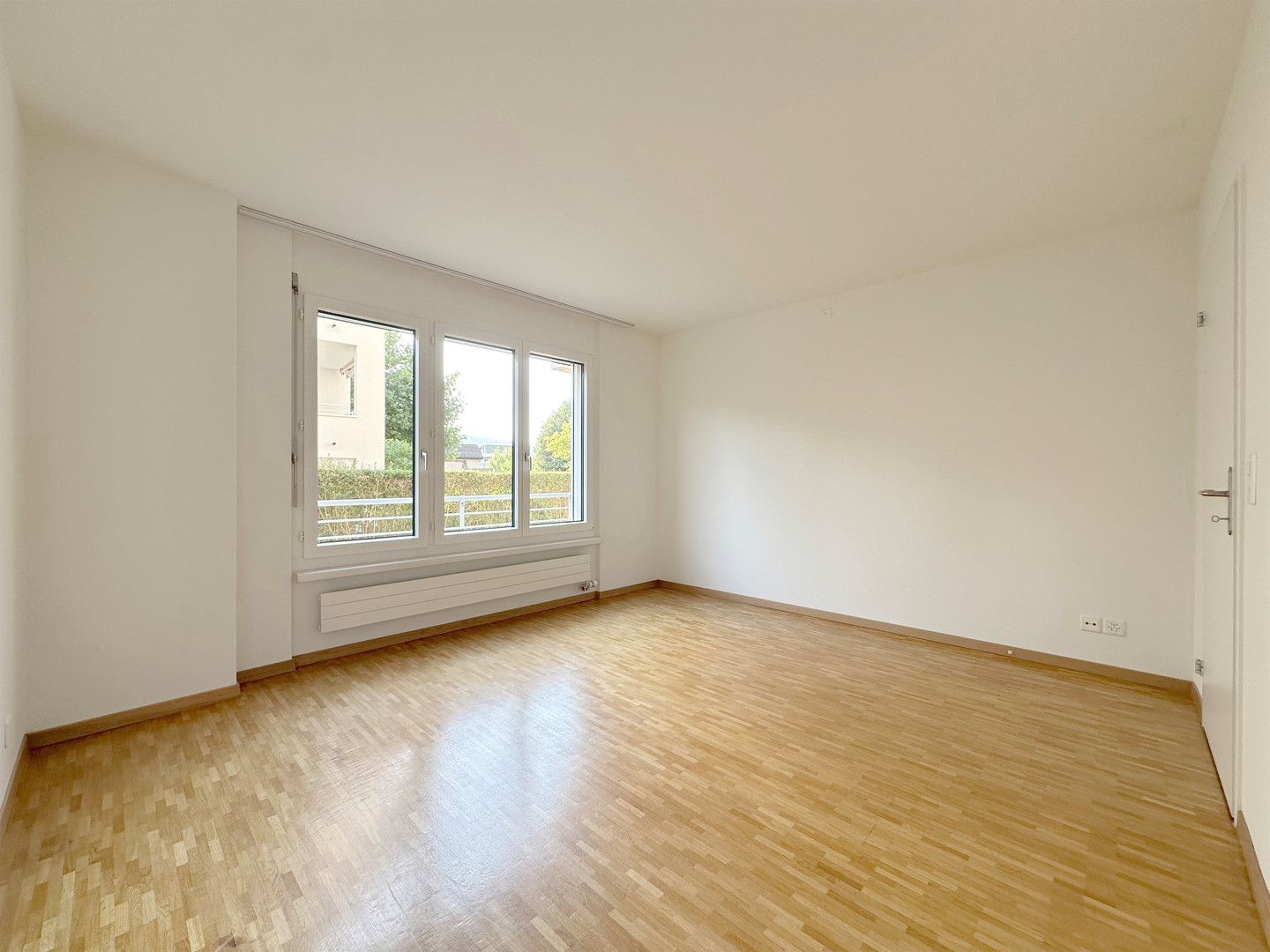 Heller, leerer Wohnraum mit Parkettboden und großem Fenster