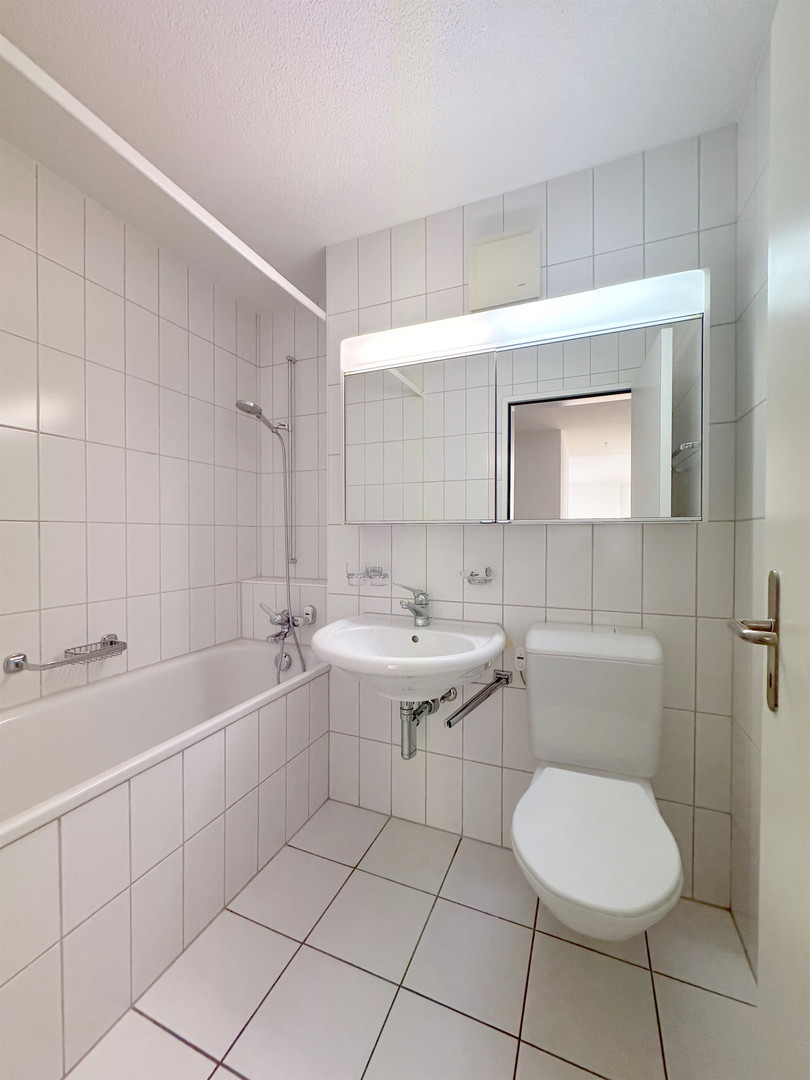 Kleines weiß gefliestes Badezimmer mit Wanne, Waschbecken und WC