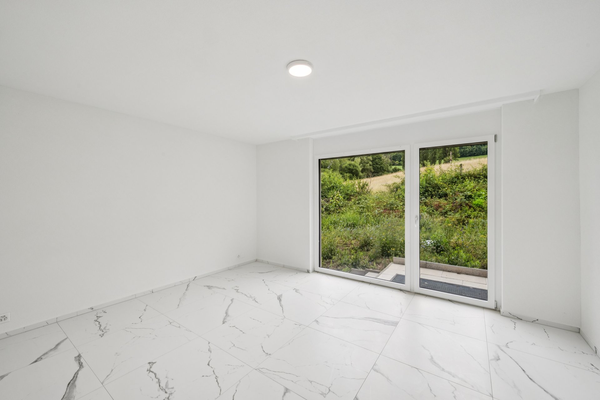 Leerer, heller Raum mit Balkon- oder Terrassentür und Grünblick