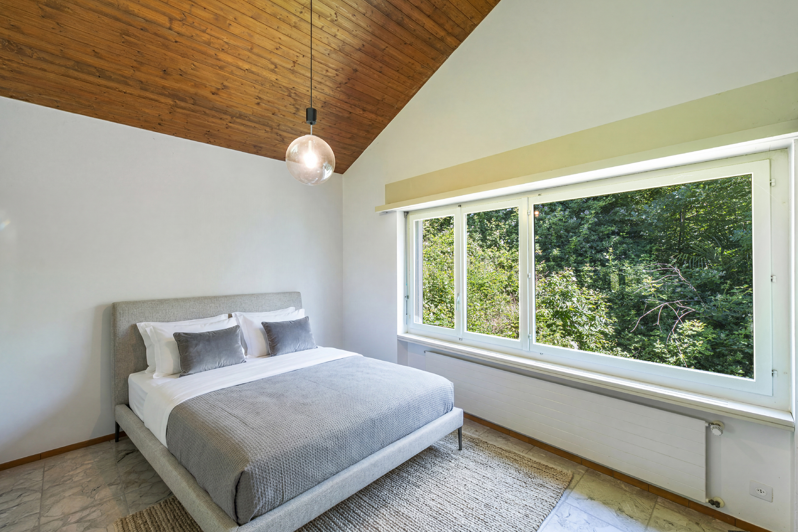 Helles Schlafzimmer mit Holzdecke und großem Fenster