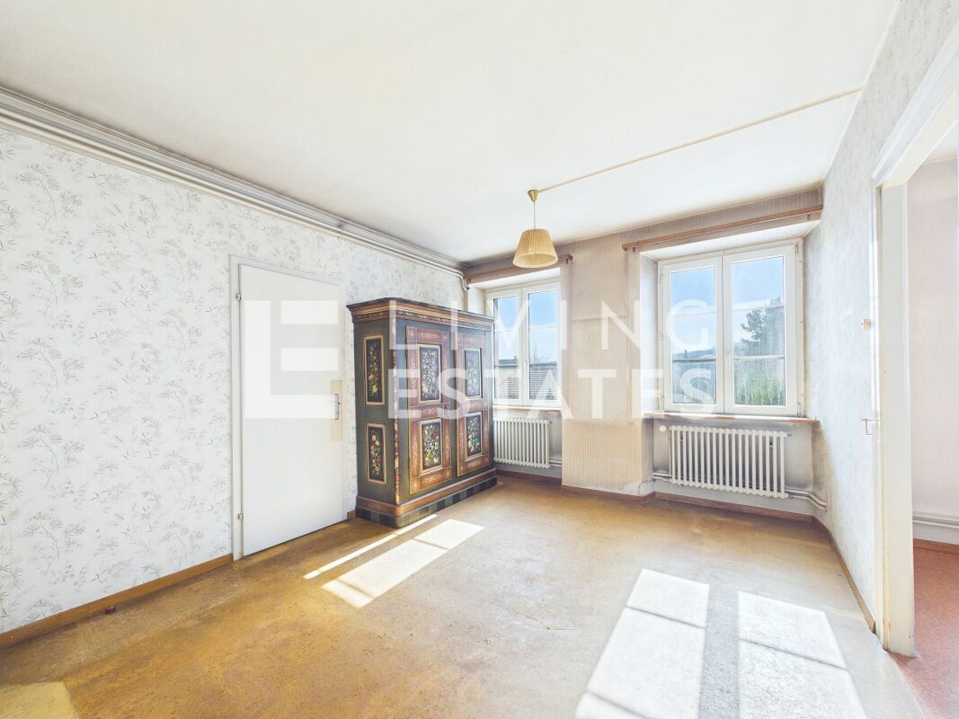 Helles, leerstehendes Zimmer mit antikem Schrank und zwei Fenstern