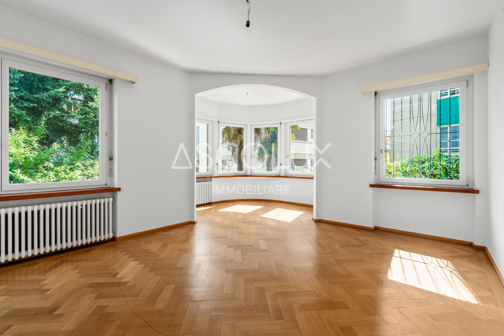 Heller leerer Wohnraum mit Parkett und großen Fenstern