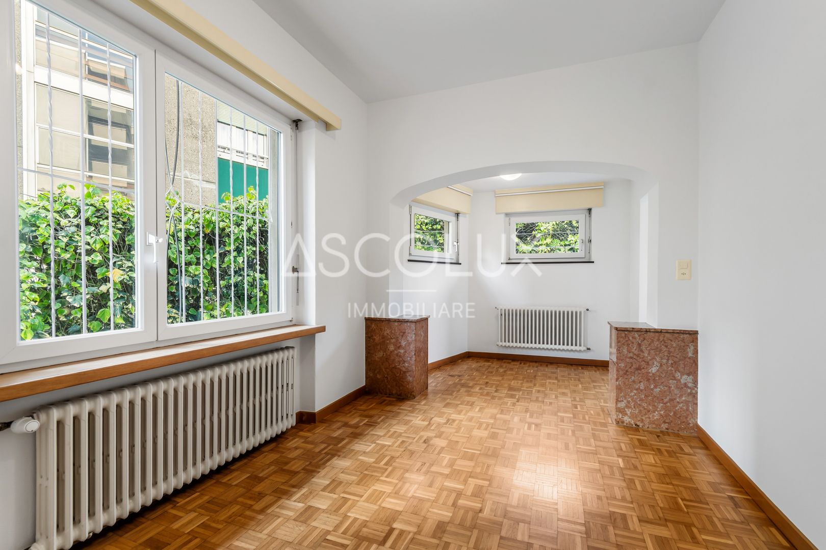 Heller leerer Wohnraum mit Parkettboden und großen Fenstern