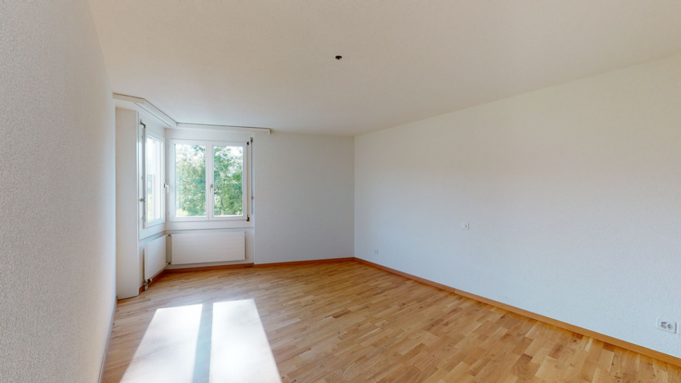 Leerer heller Wohnraum mit Parkett und Fensterfront