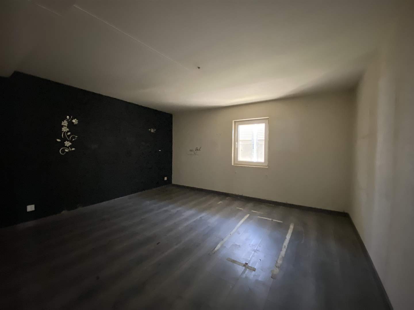 Leeres Zimmer mit dunklem Boden und kleinem Fenster