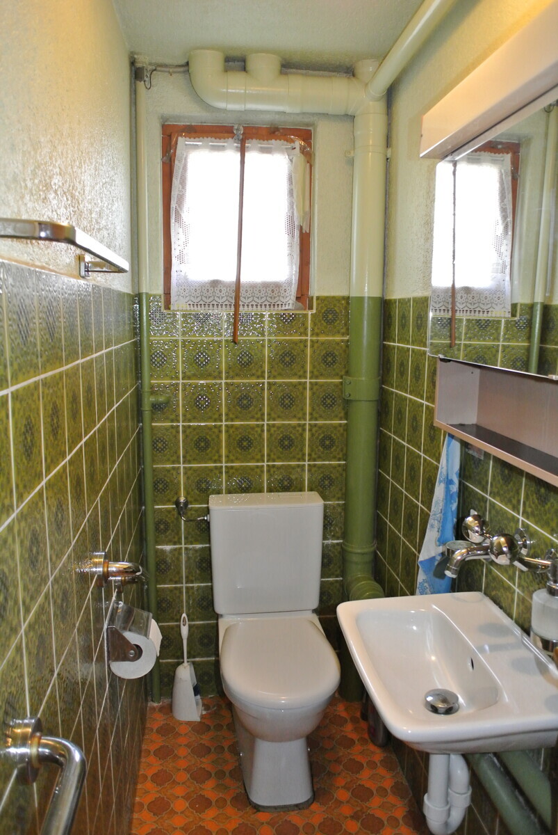 Kleines, älteres WC mit grün gefliesten Wänden
