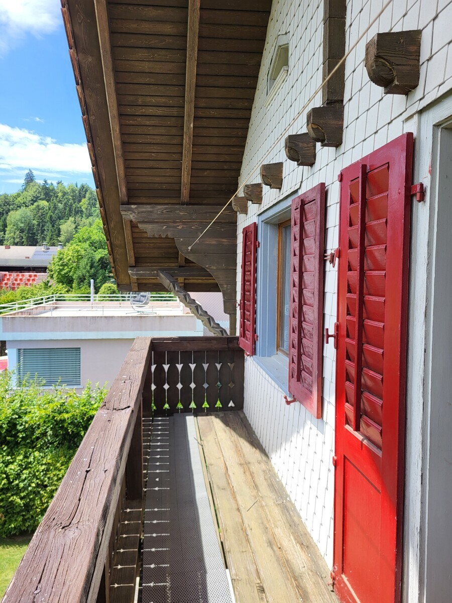 Balkon mit Holzbalken und roten Fensterläden