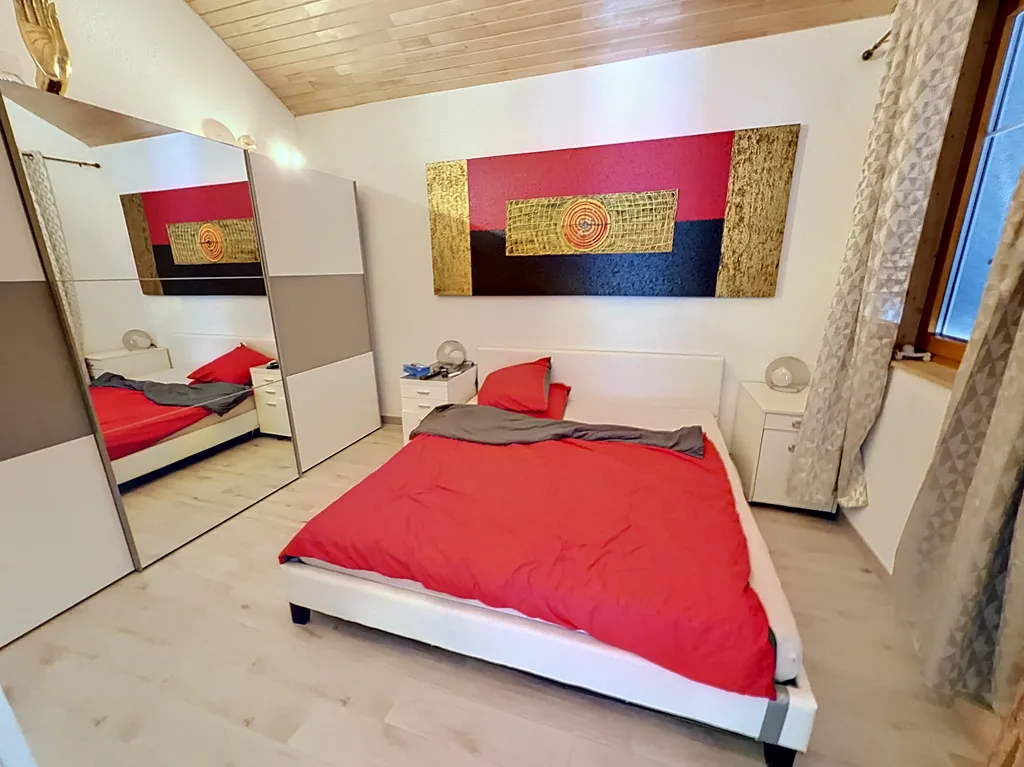 Helles Schlafzimmer mit rotem Bettbezug und großem Spiegelschrank