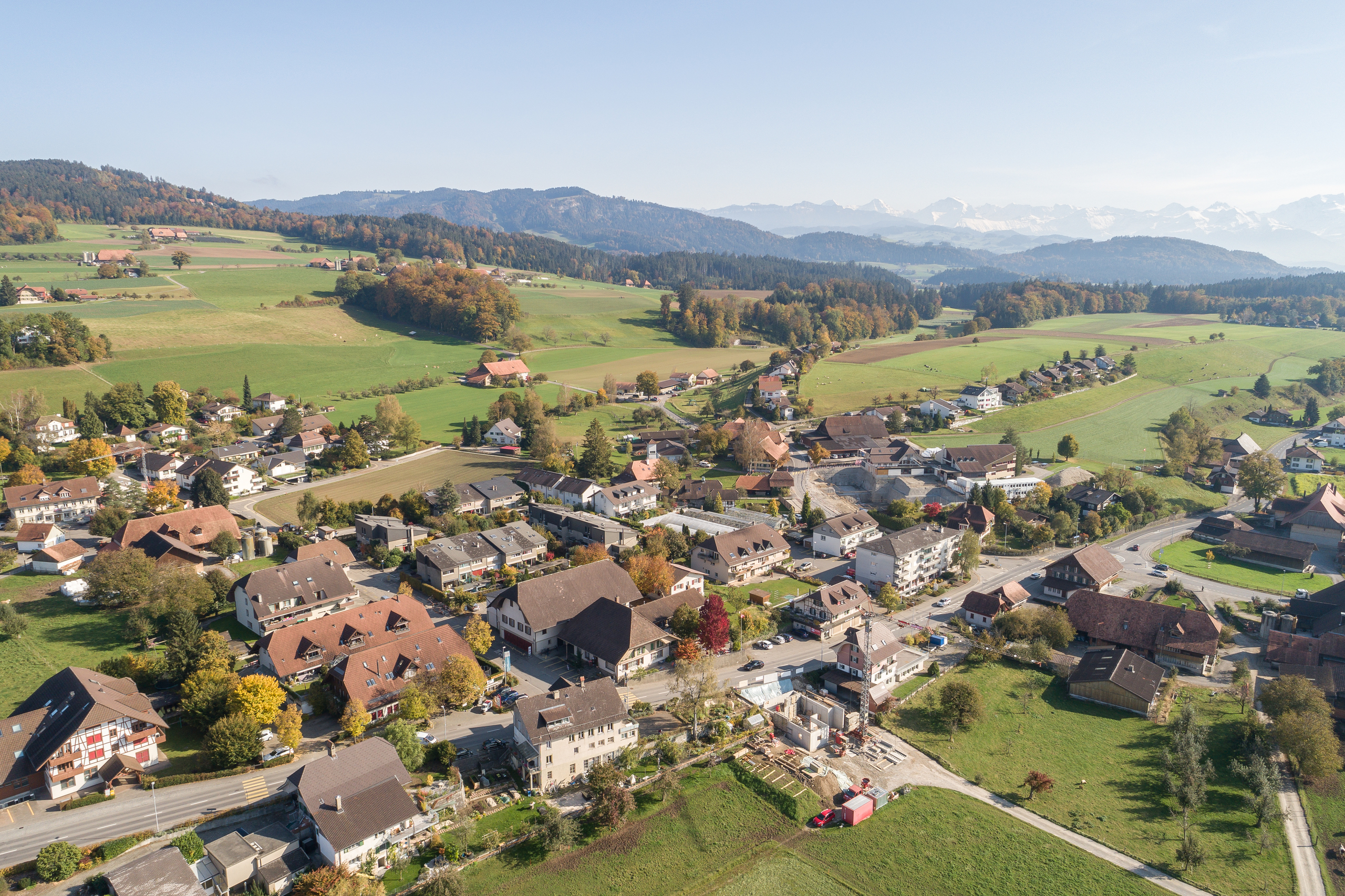 Luftaufnahme eines ländlichen Dorfes mit Alpenpanorama