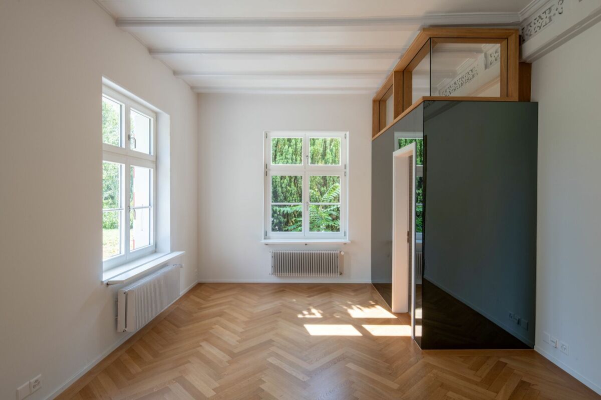Heller leerer Raum mit Parkett und hohen Fenstern