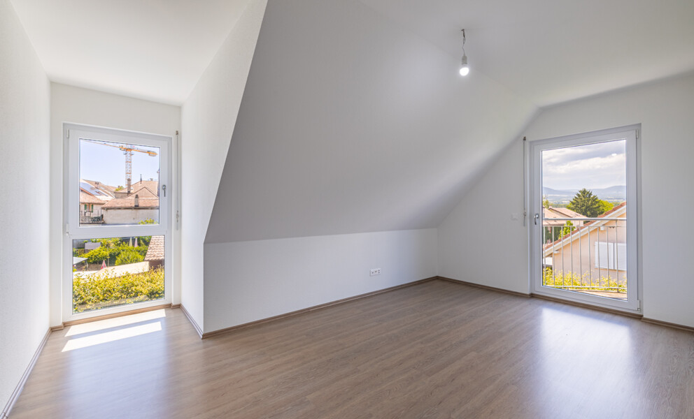 Helles, leeres Dachgeschosszimmer mit zwei Fenstern