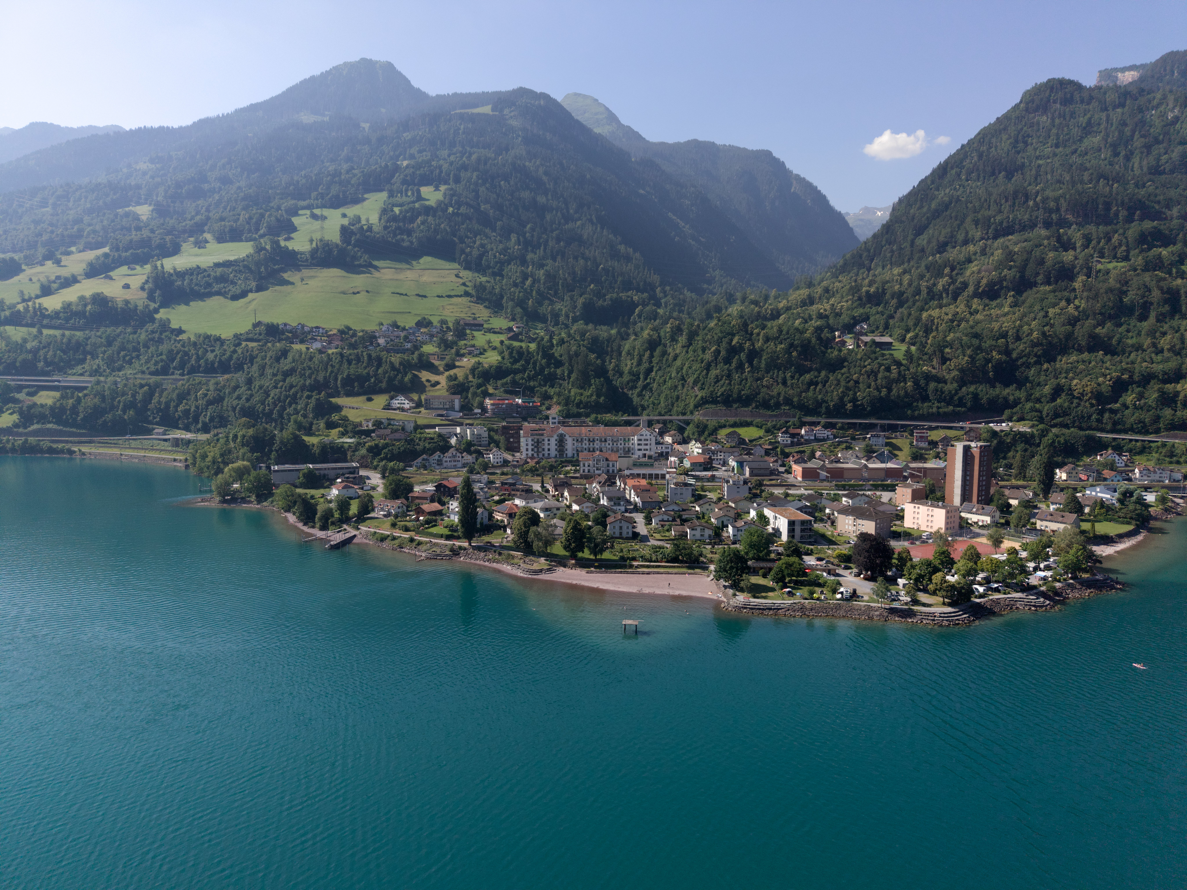 Luftaufnahme eines Sees mit Ortschaft und Bergkulisse