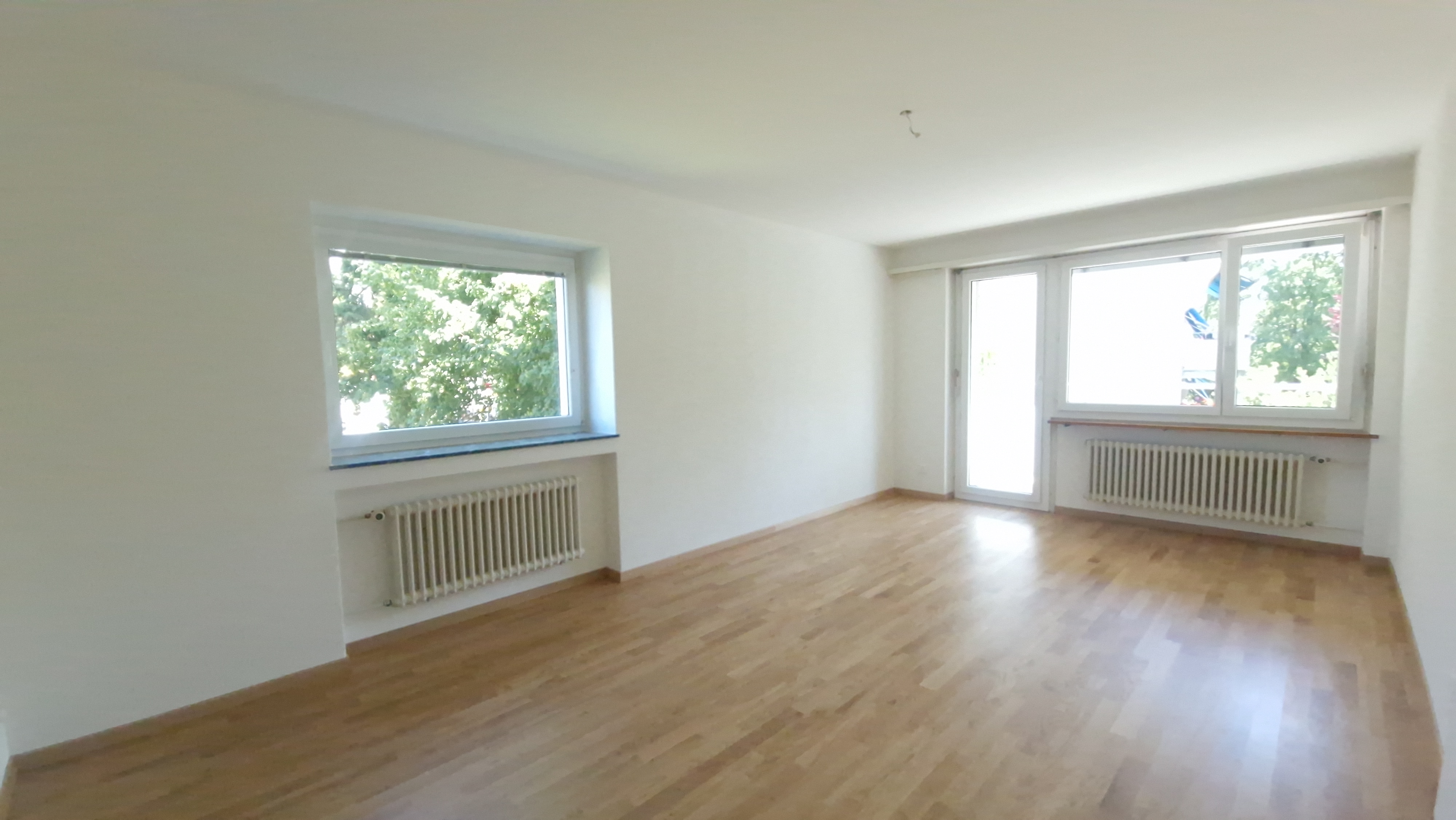 Heller leerer Wohnraum mit Parkett und Fenstern