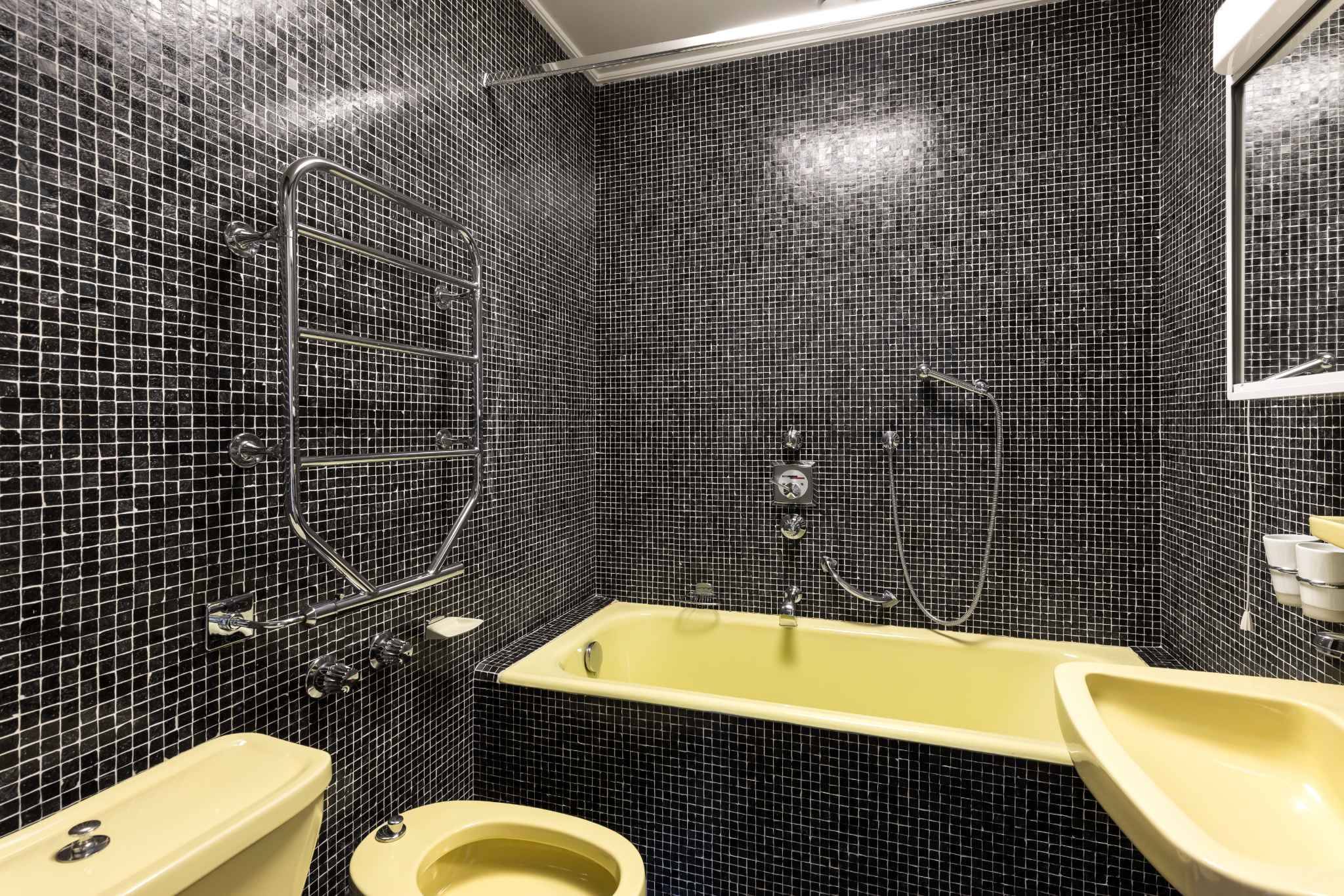 Badezimmer mit dunkler Mosaikverkleidung und gelben Sanitärkeramiken