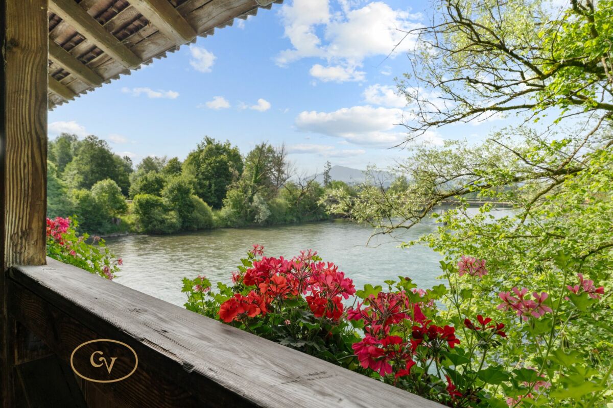 Blick von einer Holzveranda auf einen Fluss mit Blumen im Vordergrund