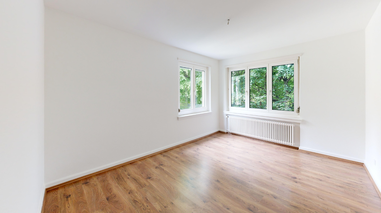 Leerer, heller Raum mit Holzfußboden und großen Fenstern