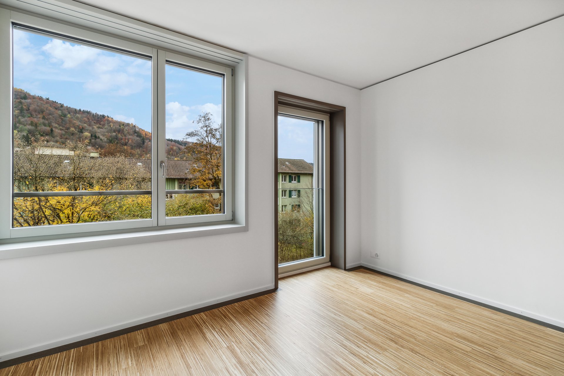 Heller leerer Raum mit großen Fenstern und Ausblick ins Grüne