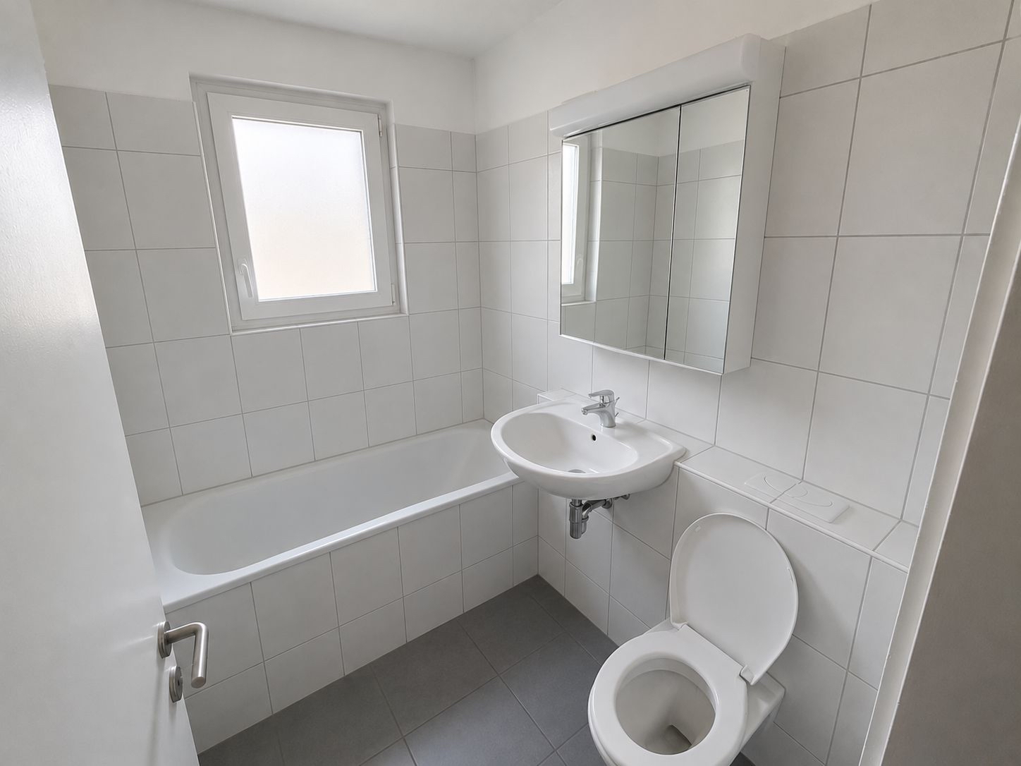 Kleines weißes Badezimmer mit Badewanne, Waschbecken und WC